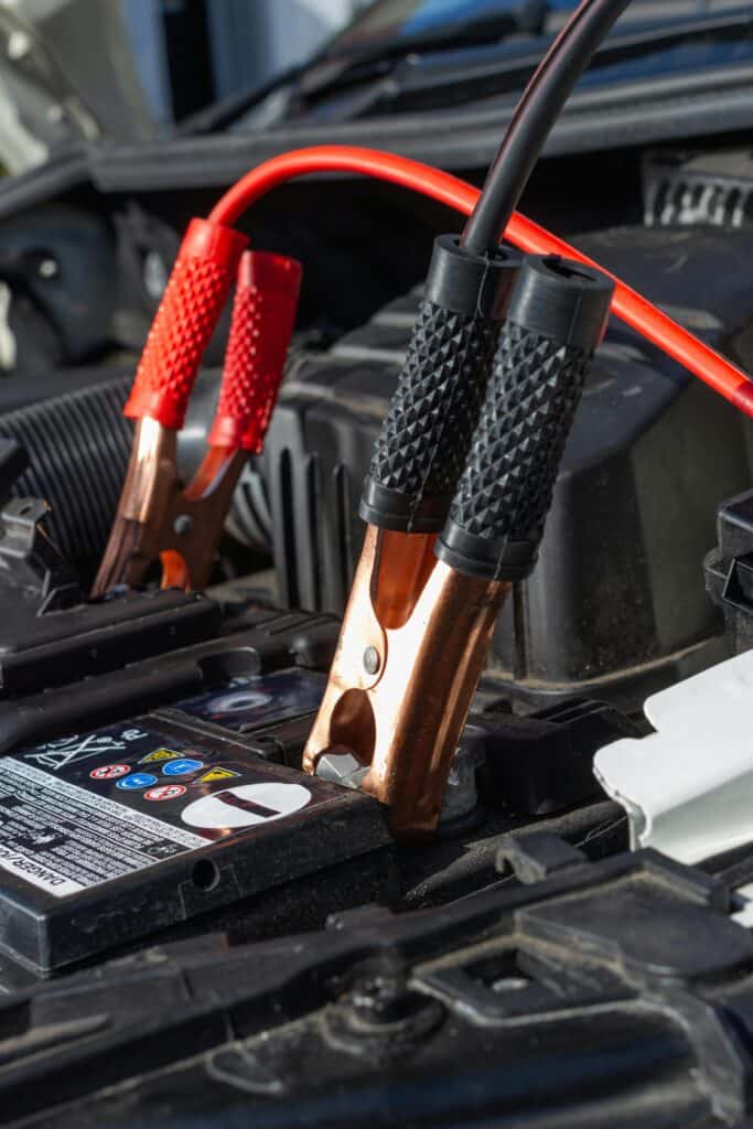 Red and black jumper cable clamps attached to the terminals of a car battery under an open hood