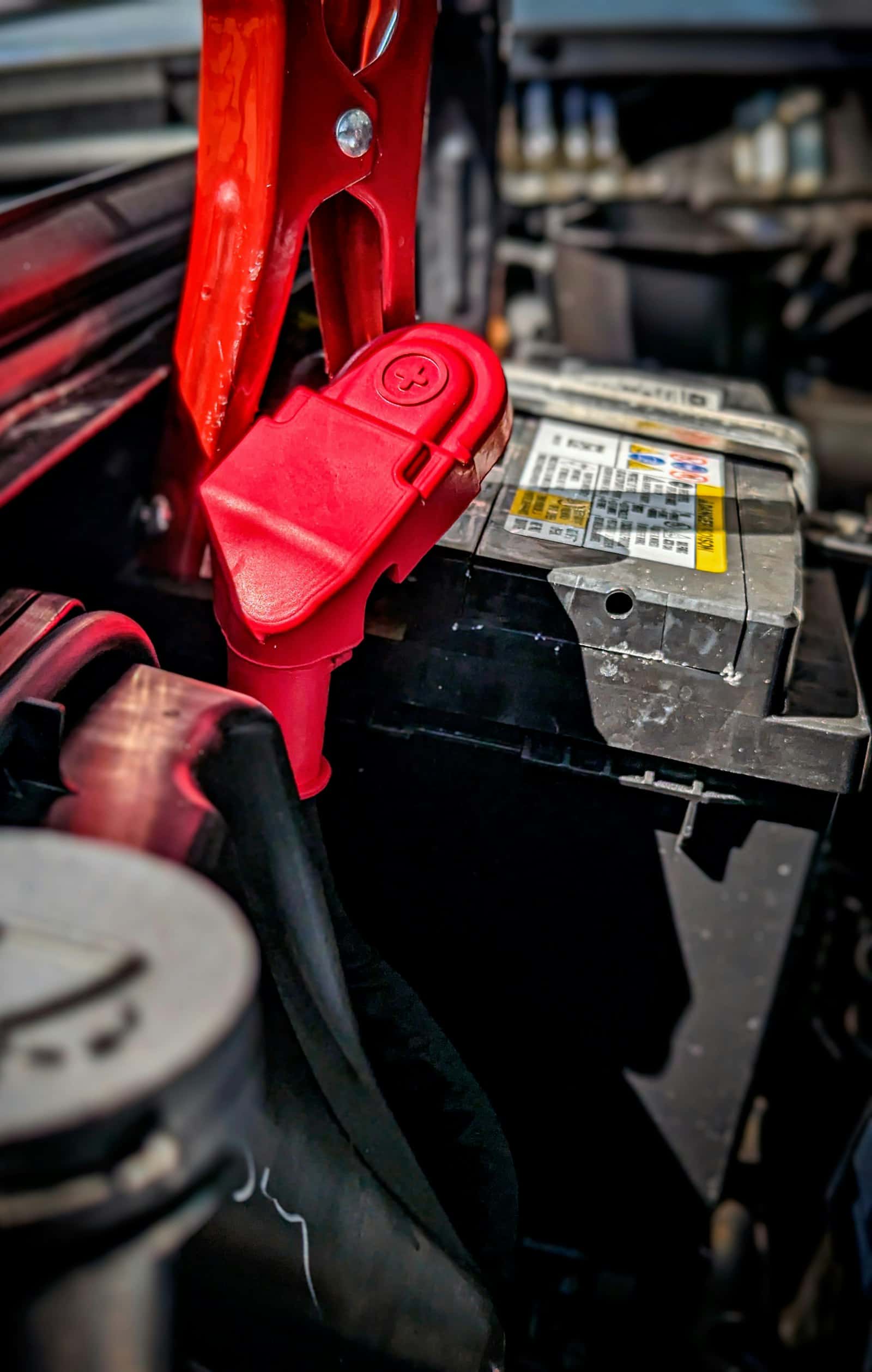 A red jumper cable clamp fastened to the positive terminal of a car battery during a jump start call in Durham Region, Ontario