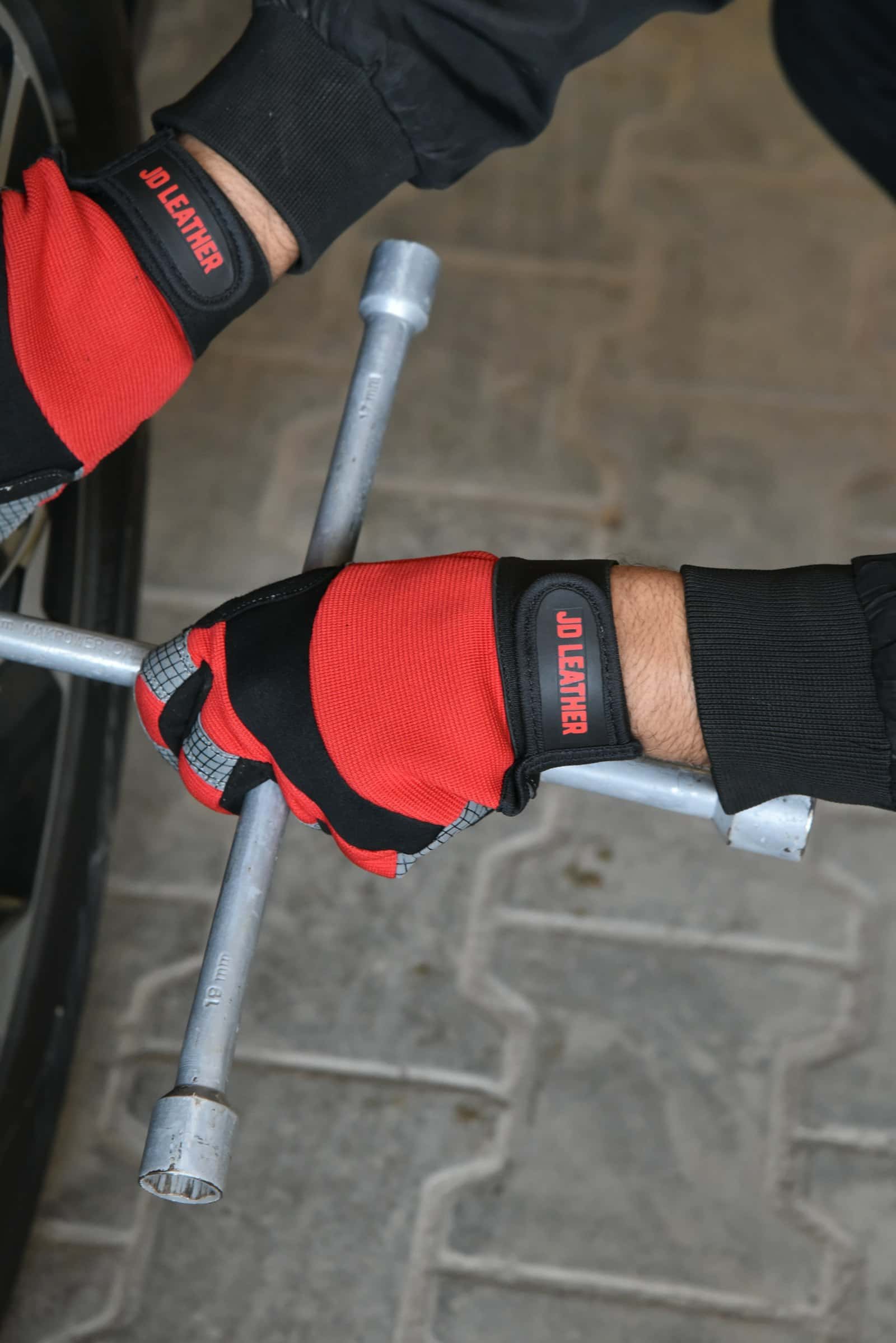 Gloved hands turning a four-way lug wrench on a wheel at a driveway kerbside, the last step of every tire change Jang does in Durham Region, Ontario