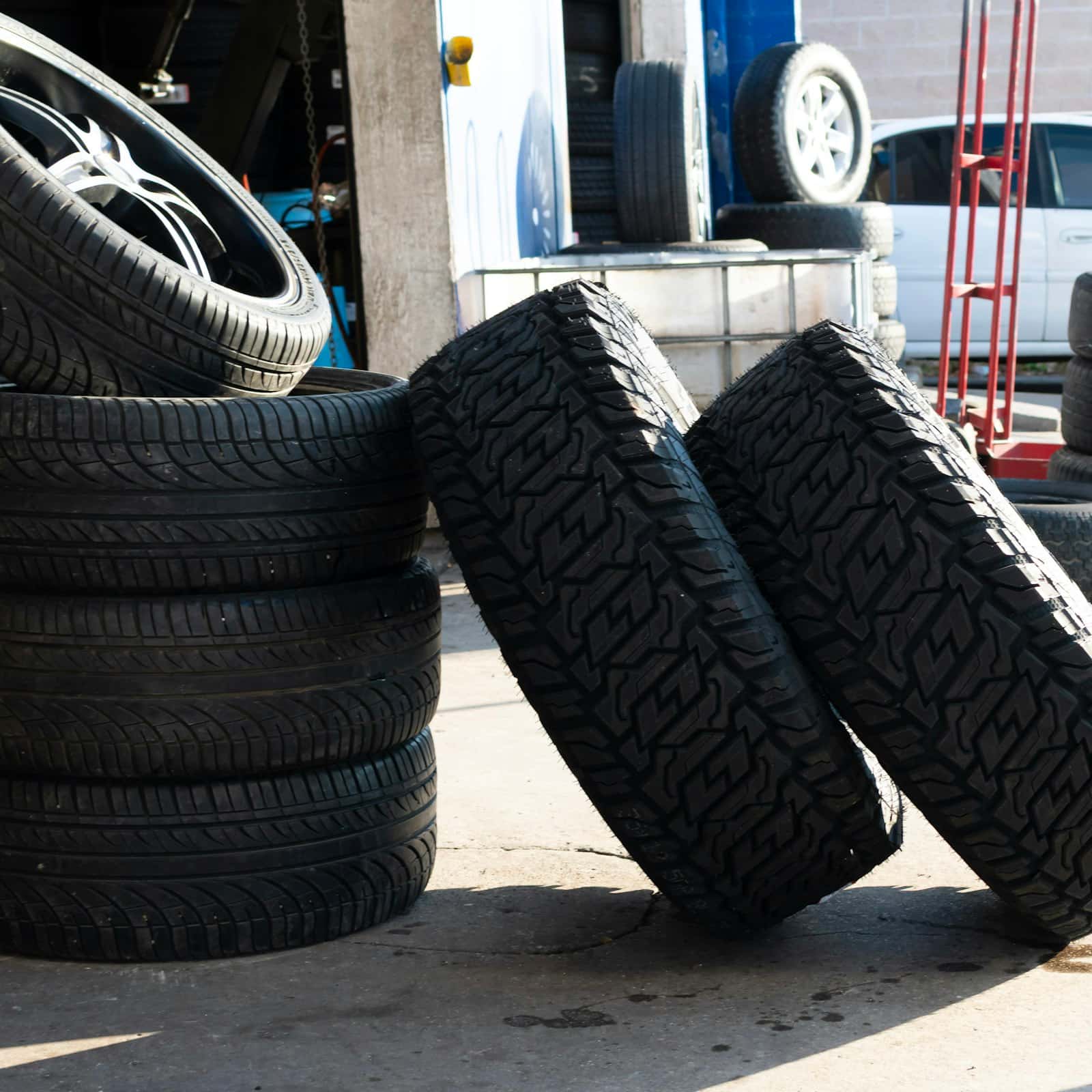 Car tires stacked and standing on the ground in daylight beside a loaded service van, the way a mobile tire fitter carries stock to a customer in Durham Region, Ontario