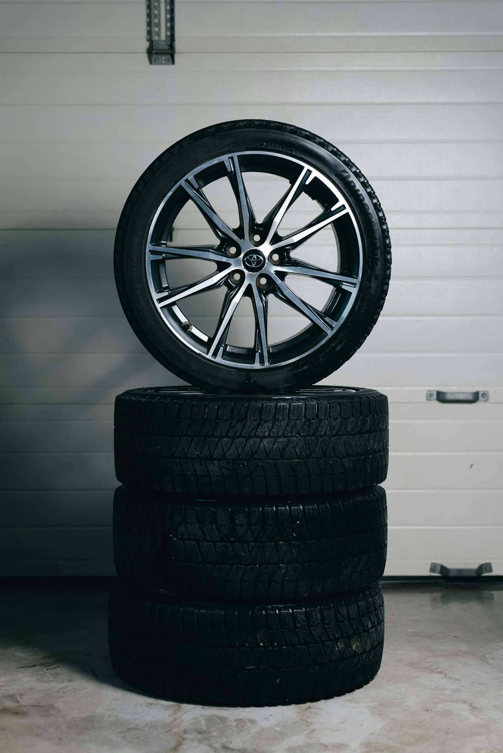 A stack of winter tires with a summer alloy wheel resting on top, the swap made twice a year on driveways across Oshawa and Durham Region, Ontario