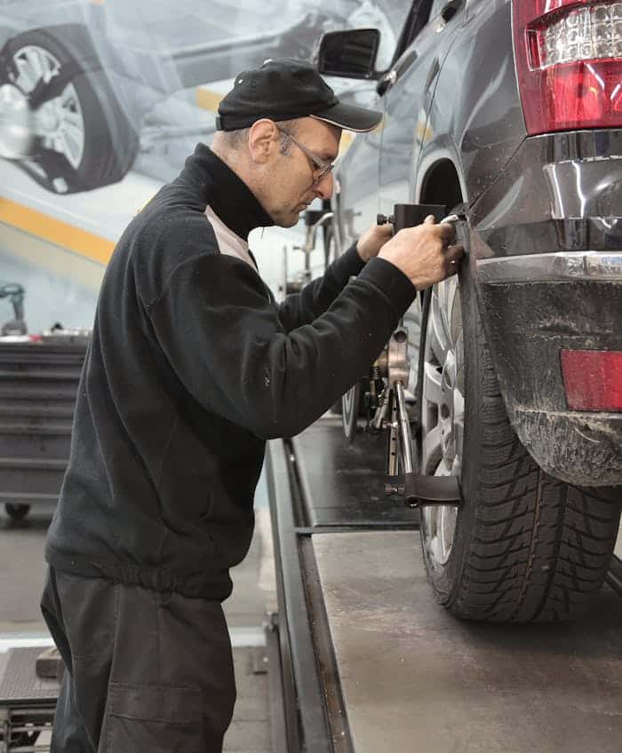 A technician fitting measuring equipment to the rear wheel of a car raised on a ramp to check the balance