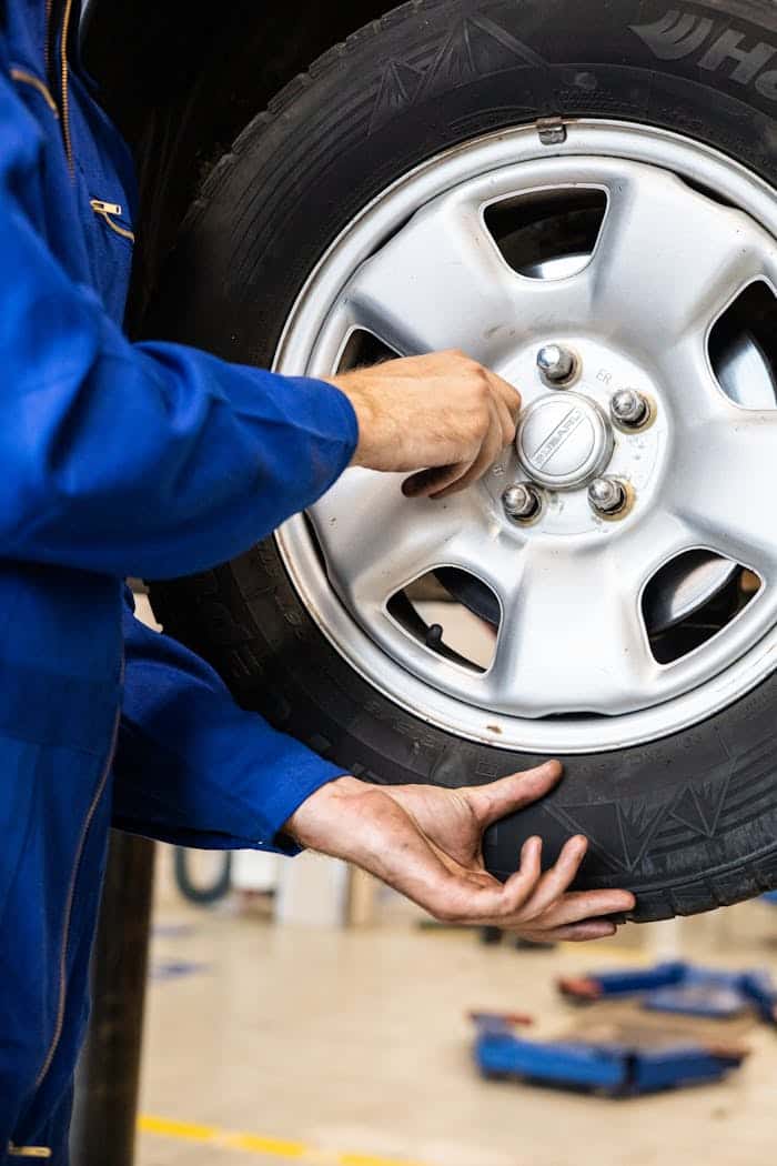 A technician guiding a wheel back onto the studs and lining up the bolt holes by hand