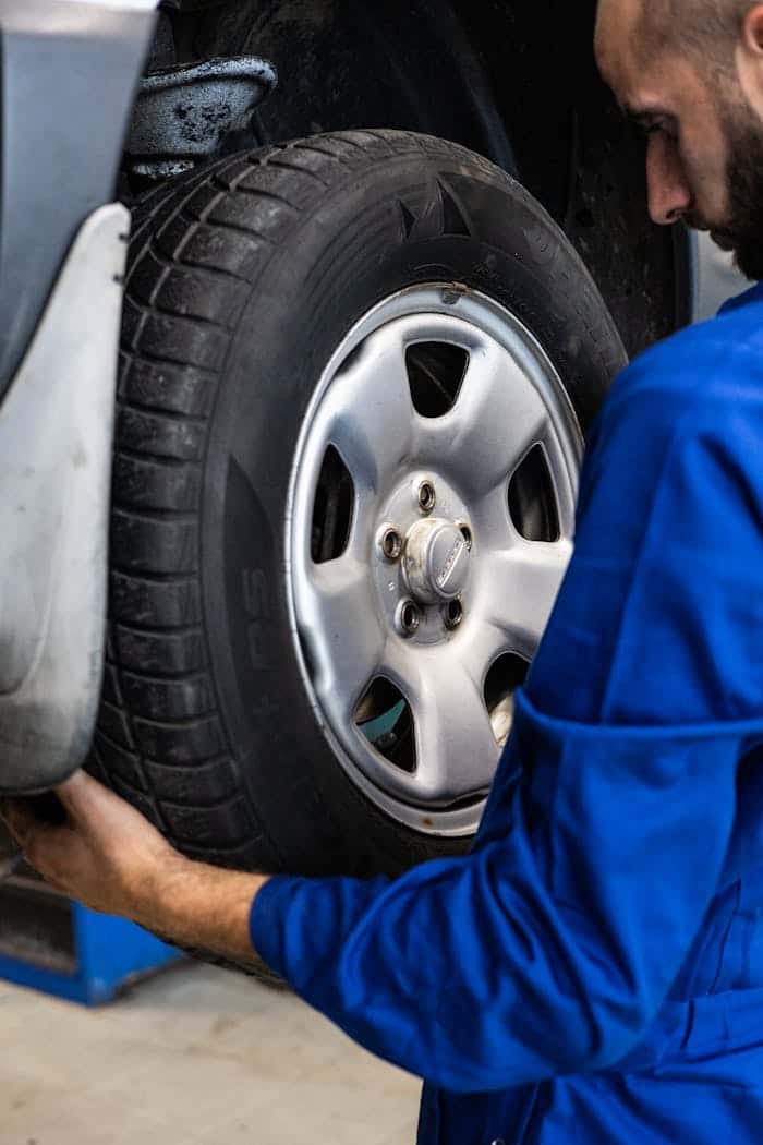 A technician in blue overalls lifting a wheel clear of the hub during a seasonal tire changeover